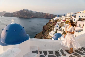 Femme en robe blanche sur une terrasse de Santorin avec vue sur la caldeira et les dômes bleus emblématiques de l'île